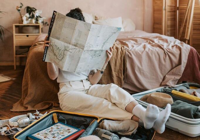 Person sitting on an open suitcase and reading a map for travel tips from a pro in a cozy bedroom