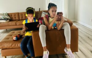 Two children using electronic devices while waiting to start a road trip.