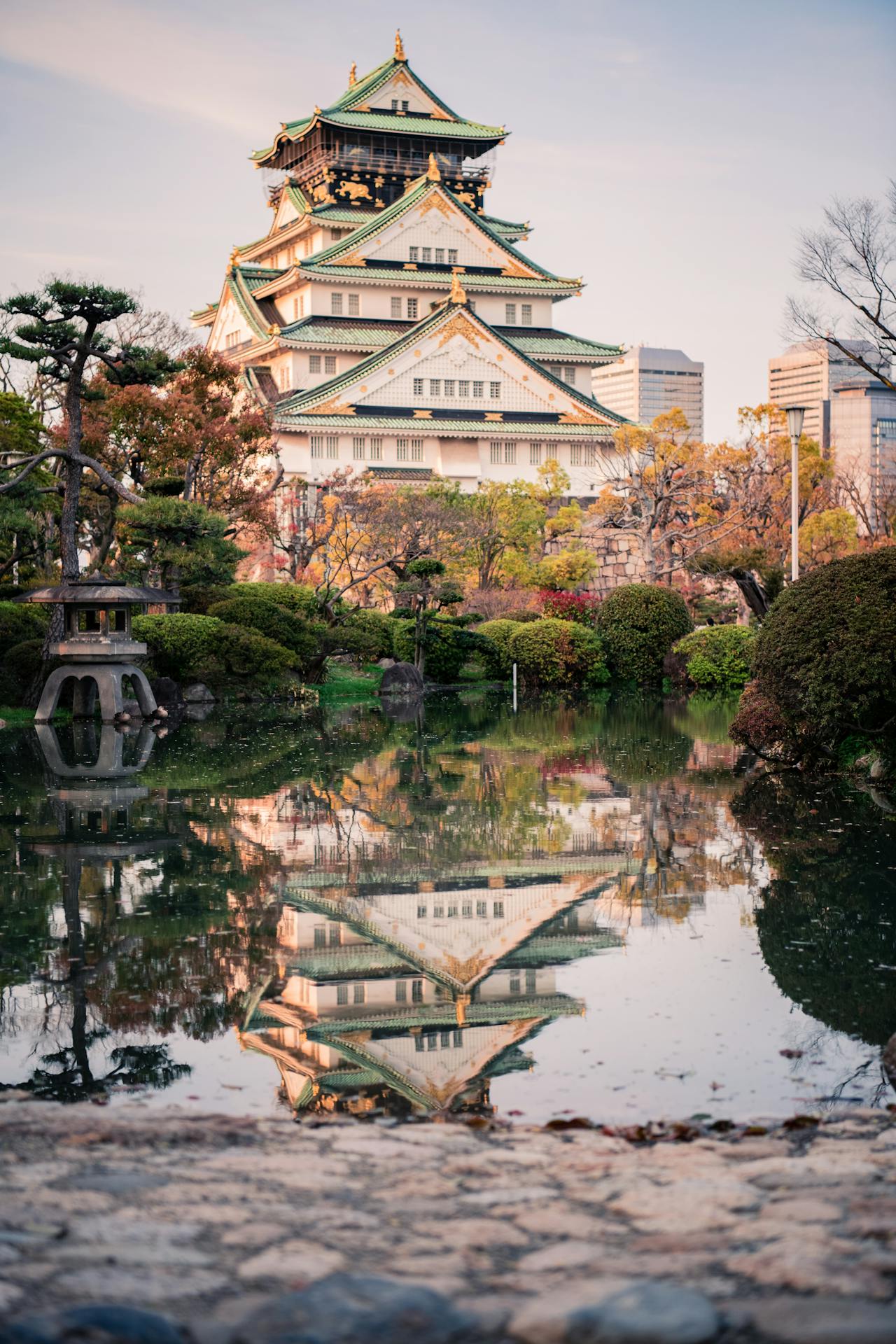 Osaka Castle reflecting in a serene pond surrounded by lush greenery during autumn.