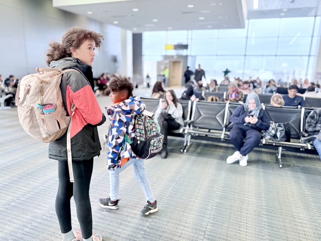 Kids waiting at the airport with backpacks, preparing for a family-friendly D.C. itinerary.